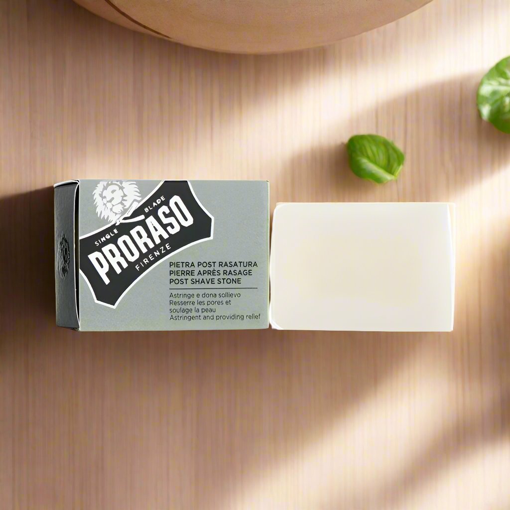 A 100g Proraso After Shave Stone. The packaging features a white and green color scheme with a transparent window showcasing the natural alum stone inside. The label displays the product name and brand.
