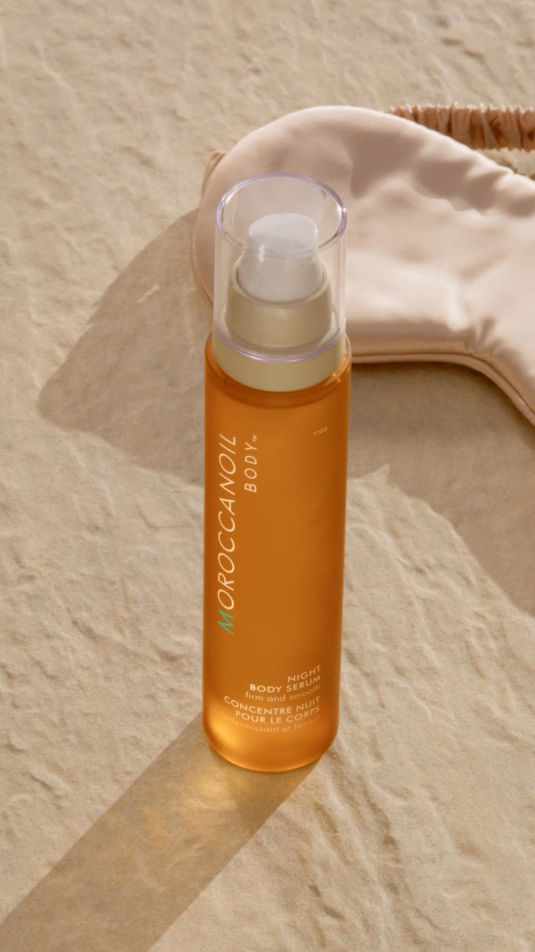Orange bottle of MOROCCANOIL Body oil on a beige sand background