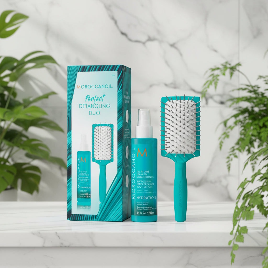 Moroccanoil Perfect Detangling Duo set featuring a teal and black packaging box, a matching detangling spray bottle, and a paddle hairbrush on a marble white background.