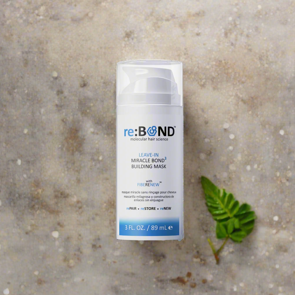 re:BOND leave-in building mask bottle on a textured surface with a green leaf