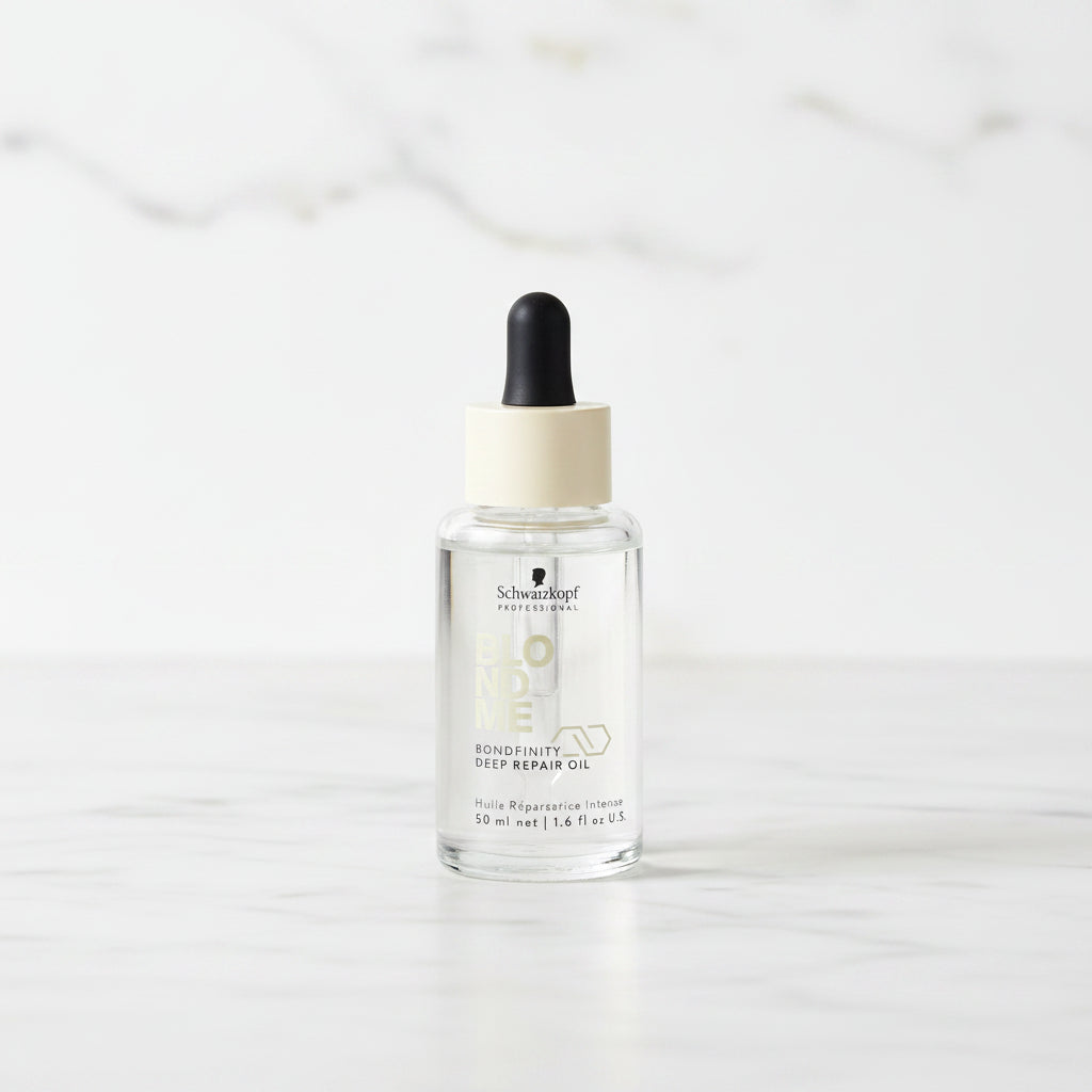 Bottle of 'Blond Me' hair product with dropper on a marble surface with plants in the background