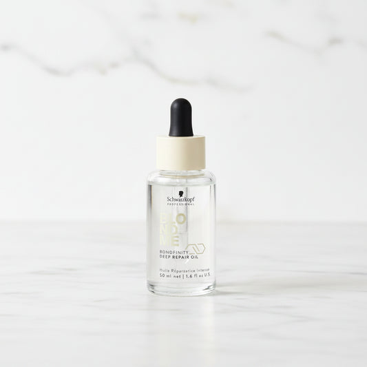 Bottle of 'Blond Me' hair product with dropper on a marble surface with plants in the background